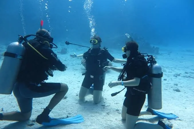 Instructor and two students kneeling on a sandy seabed during an underwater skills session.