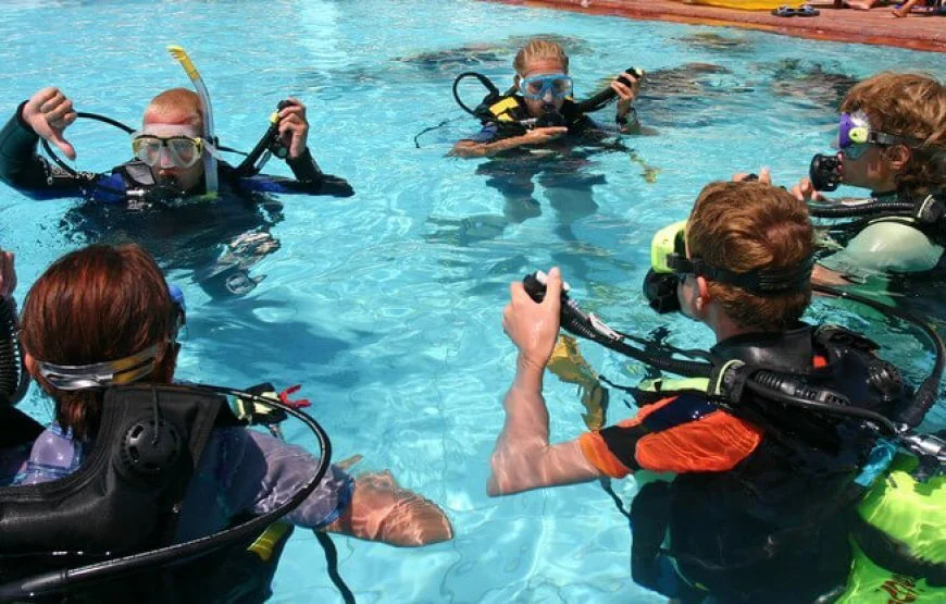 Instructor and four students standing in a loose circle in a swimming pool practicing skills together.