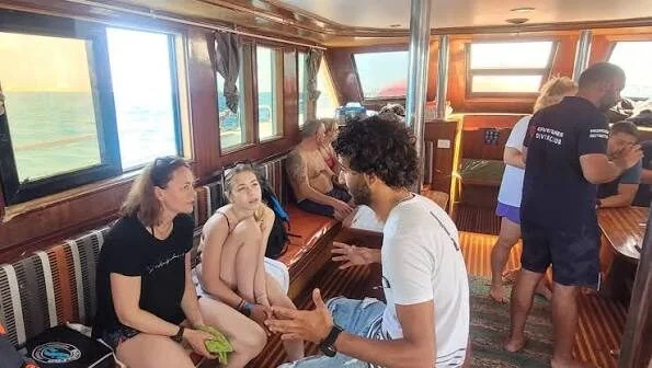 مجموعة طلاب ومدرب يجلسون في صالون القارب المظلل المكسو بالخشب أثناء إحاطة