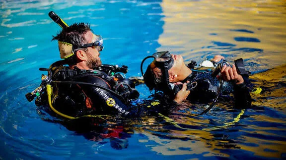 Zwei Taucher üben im Schwimmbecken an der Oberfläche gemeinsam eine Rettungstechnik