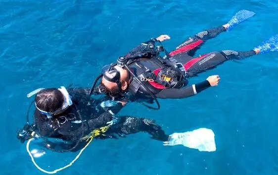 Taucher schleppt bei einer Rettungsübung einen anderen Taucher am Flaschenventil über die Wasseroberfläche