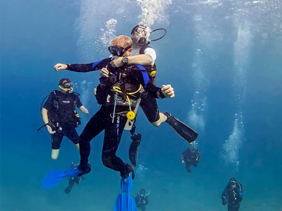 Unter Wasser stützt ein Taucher einen schlaffen Taucher und hebt ihn zur Oberfläche, Luftblasen steigen auf