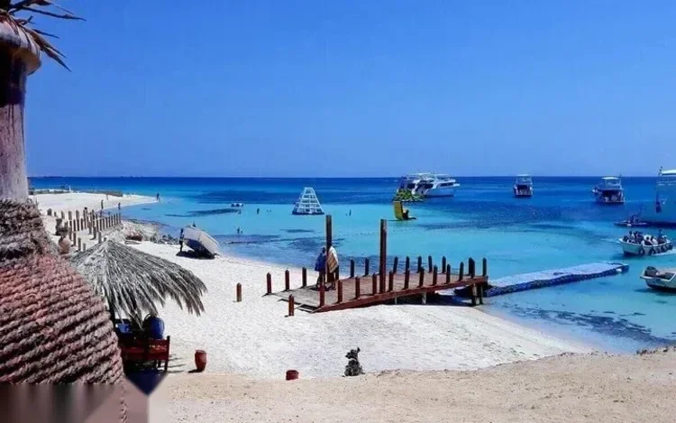 Houten steiger naar afgemeerde boten en een ondiepe turquoise lagune, gezien onder een rieten parasolluifel