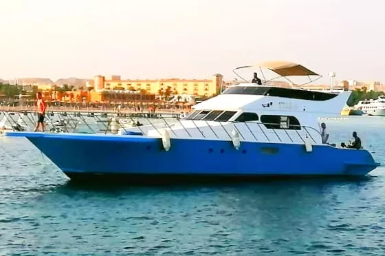 Blauw-wit motorjacht vaart bij laat middaglicht langs een kust vol hotels