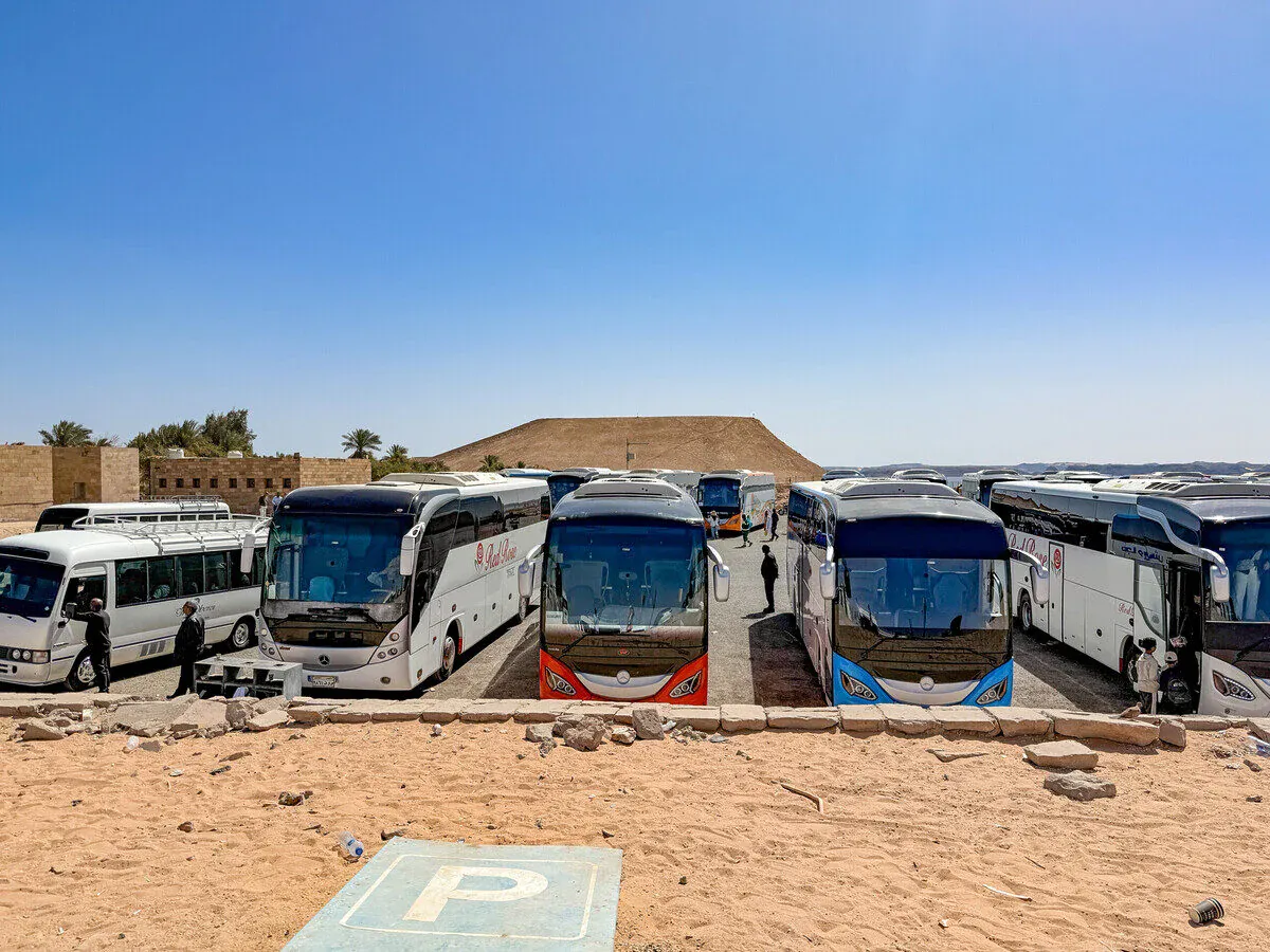 Reihen von Reisebussen auf einem Wüstenparkplatz bei Abu Simbel, dahinter Sandhügel und Palmen