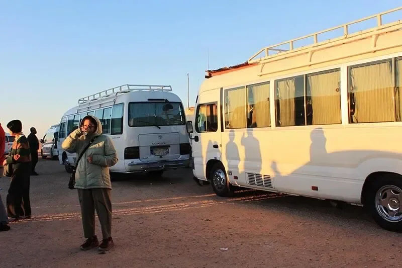 Reisender im dicken Wintermantel wartet im niedrigen Morgenlicht neben Minibussen, lange Schatten auf dem Boden