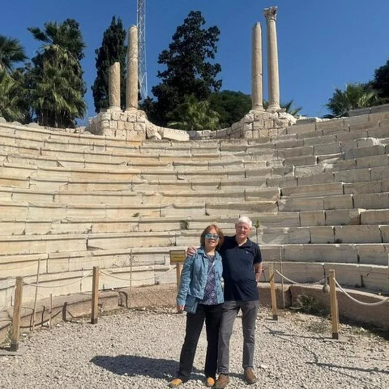 Paar zwischen den Kalksteinrängen des römischen Amphitheaters Kom el-Dikka in Alexandria, dahinter Säulen und Palmen