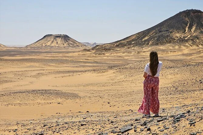 Frau steht allein und blickt über die Sandebene der Schwarzen Wüste auf dunkle Vulkanhügel