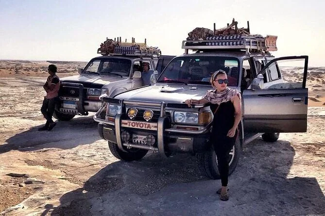 Frau posiert neben zwei beladenen Safari-Geländewagen in der Schwarzen Wüste, bei einem ist die Tür offen