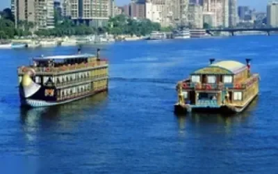 سفينتان نيليتان تقليديتان متعددتا الطوابق كمطعمين عائمين تبحران في النهر نهارًا، وأفق القاهرة في الخلفية
