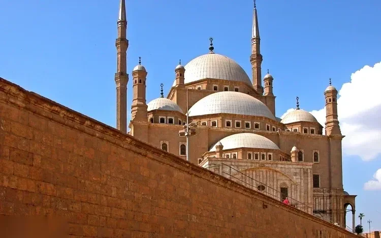 فناء مسجد محمد علي بنافورة الوضوء المركزية ومئذنتيه التوأمين ترتفعان في سماء غائمة جزئيًا