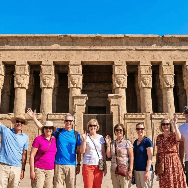 Tour group posing and waving in front of the Hathor-headed columns on the facade of Dendera Temple.