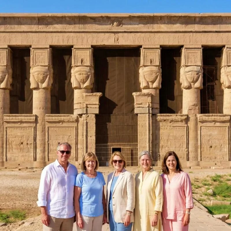 Small group of visitors standing in front of the Hathor-headed column facade of Dendera Temple.