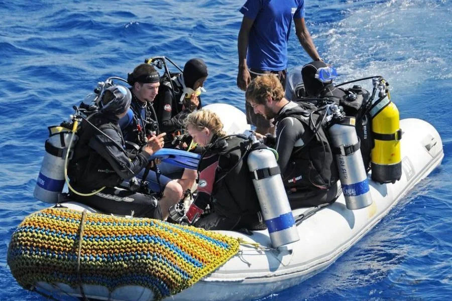 مجموعة غواصين يجلسون في قارب مطاطي يستعدون للنزول إلى الماء