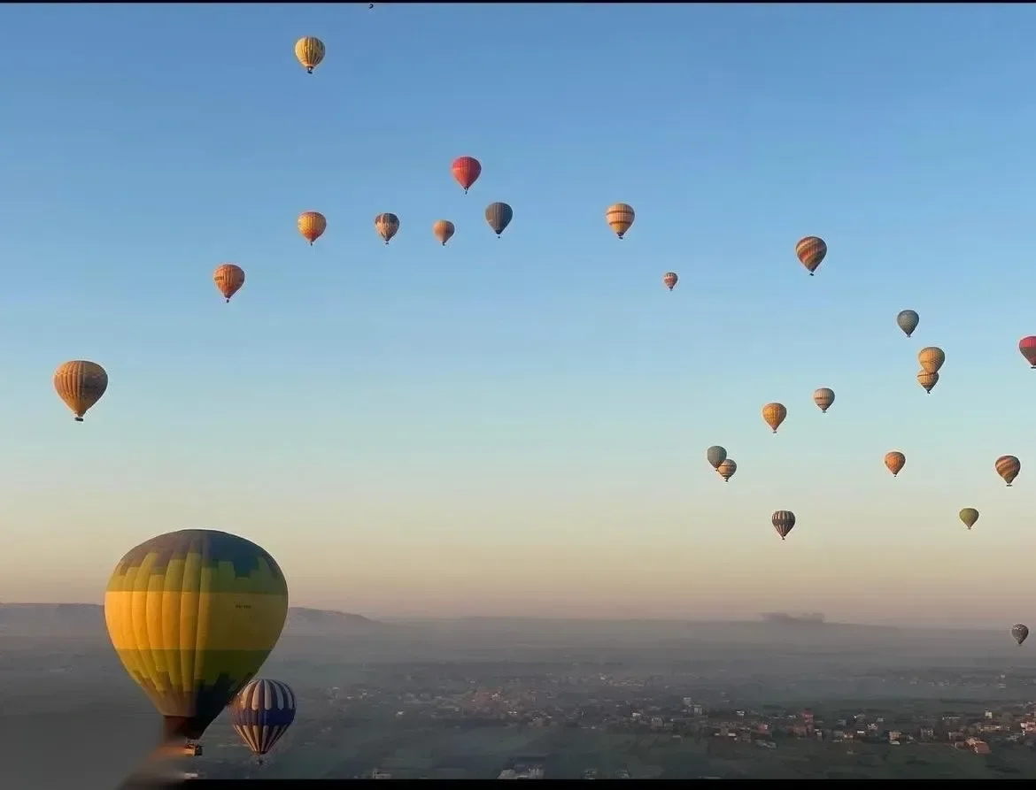 Dozens of hot air balloons scattered across the sky over the Luxor valley at sunrise