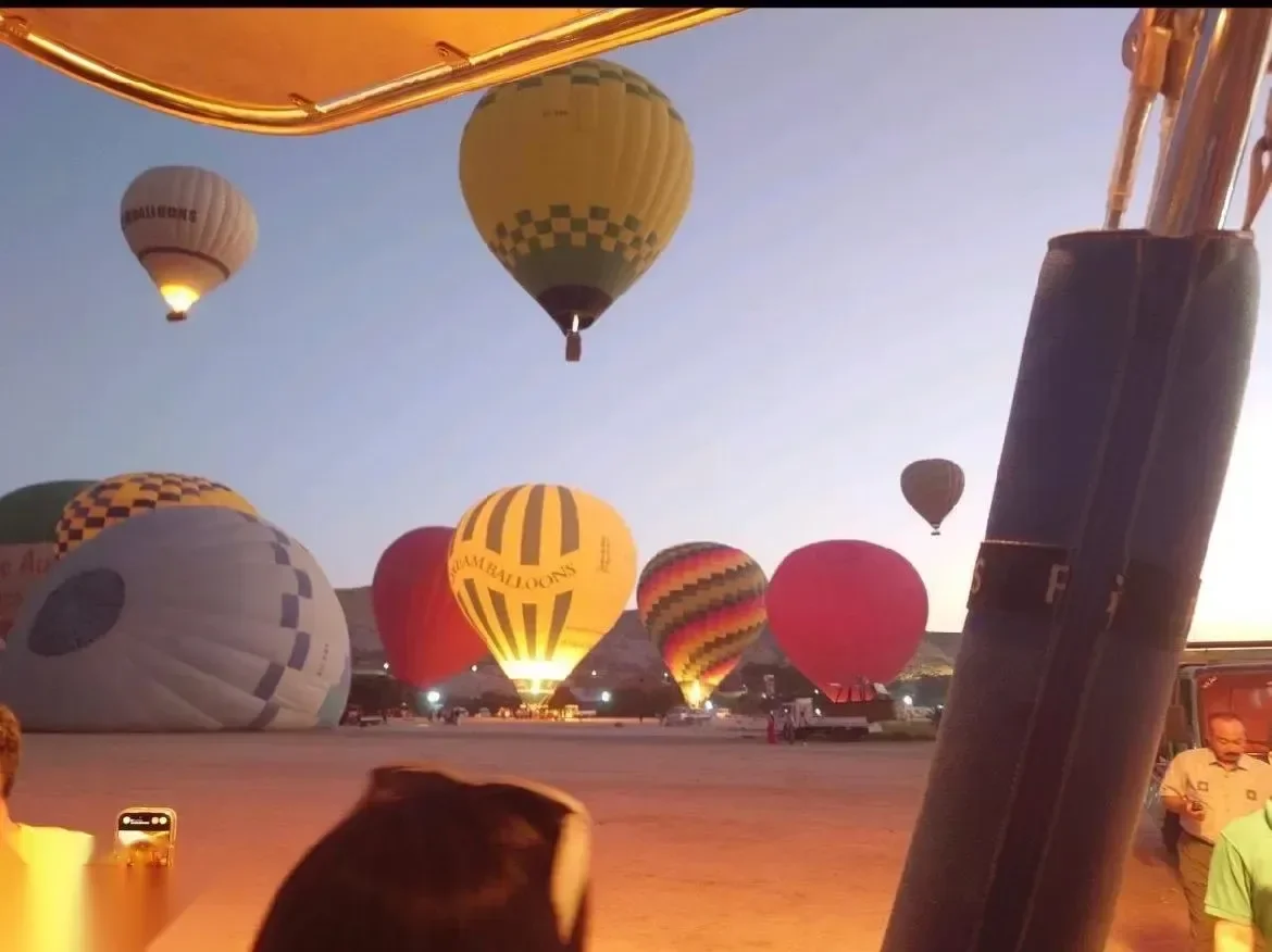 Several hot air balloons inflating on the launch field before dawn, glowing orange from their burners.
