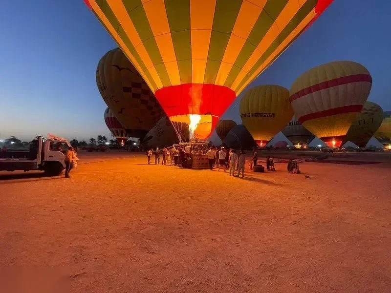 A hot air balloon crew inflating a balloon with its burner flame lit at dawn, a truck and ground staff nearby.