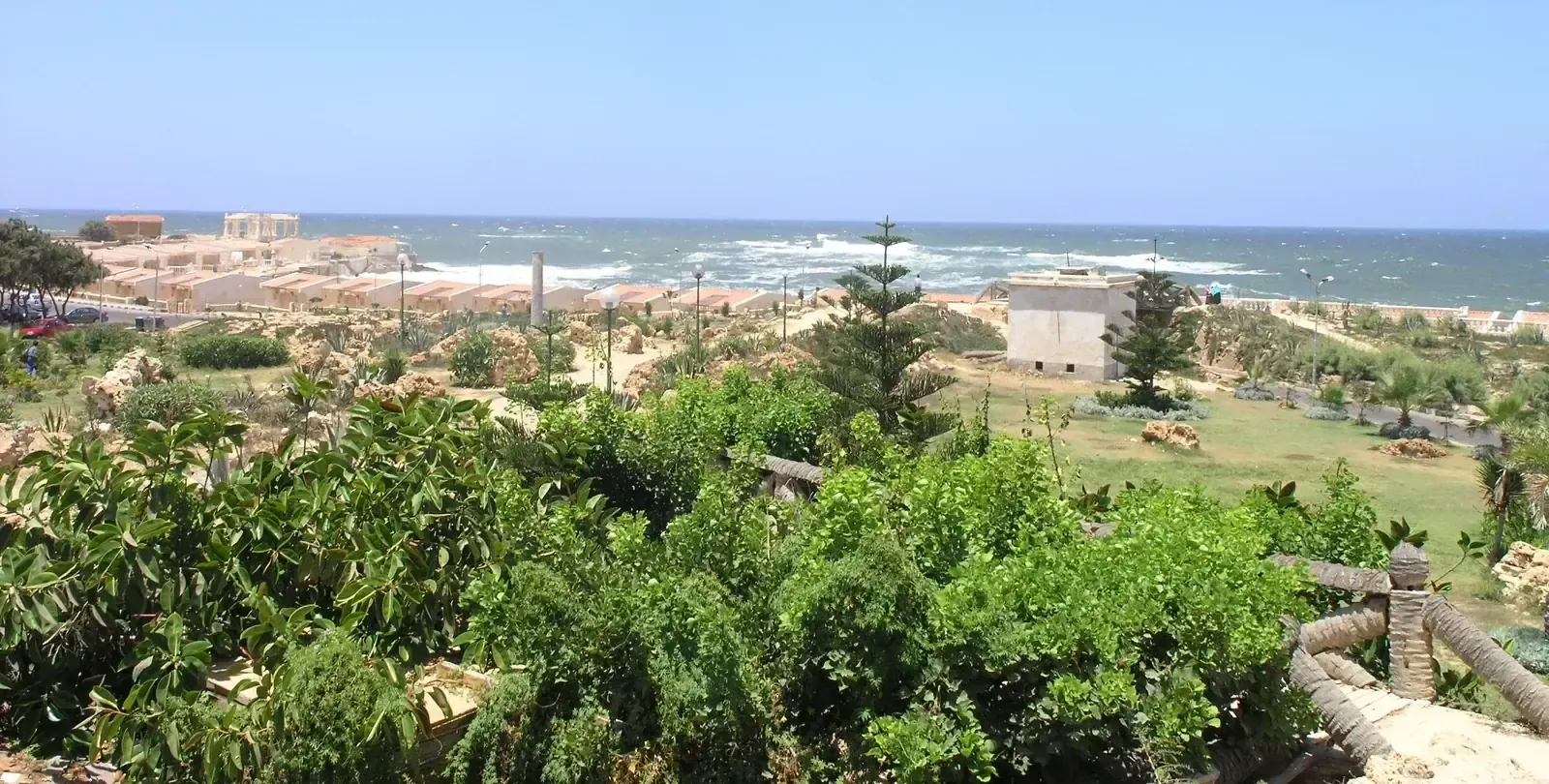 A hillside garden overlooks a row of seaside chalets and a wave-battered coastline near Montaza.