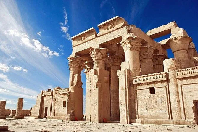 Trajan's Kiosk at Philae Temple stands with its tall columns and floral capitals under a bright blue sky with wispy clouds.