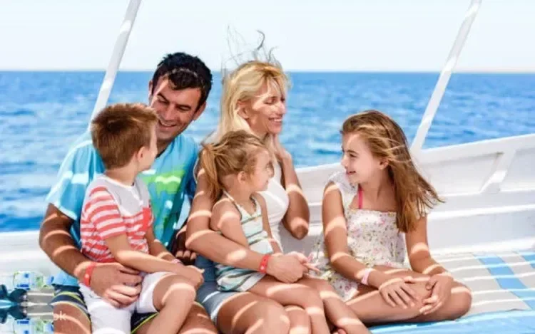 Familie mit zwei Erwachsenen und drei Kindern lacht gemeinsam auf dem Deck einer Segelyacht auf See