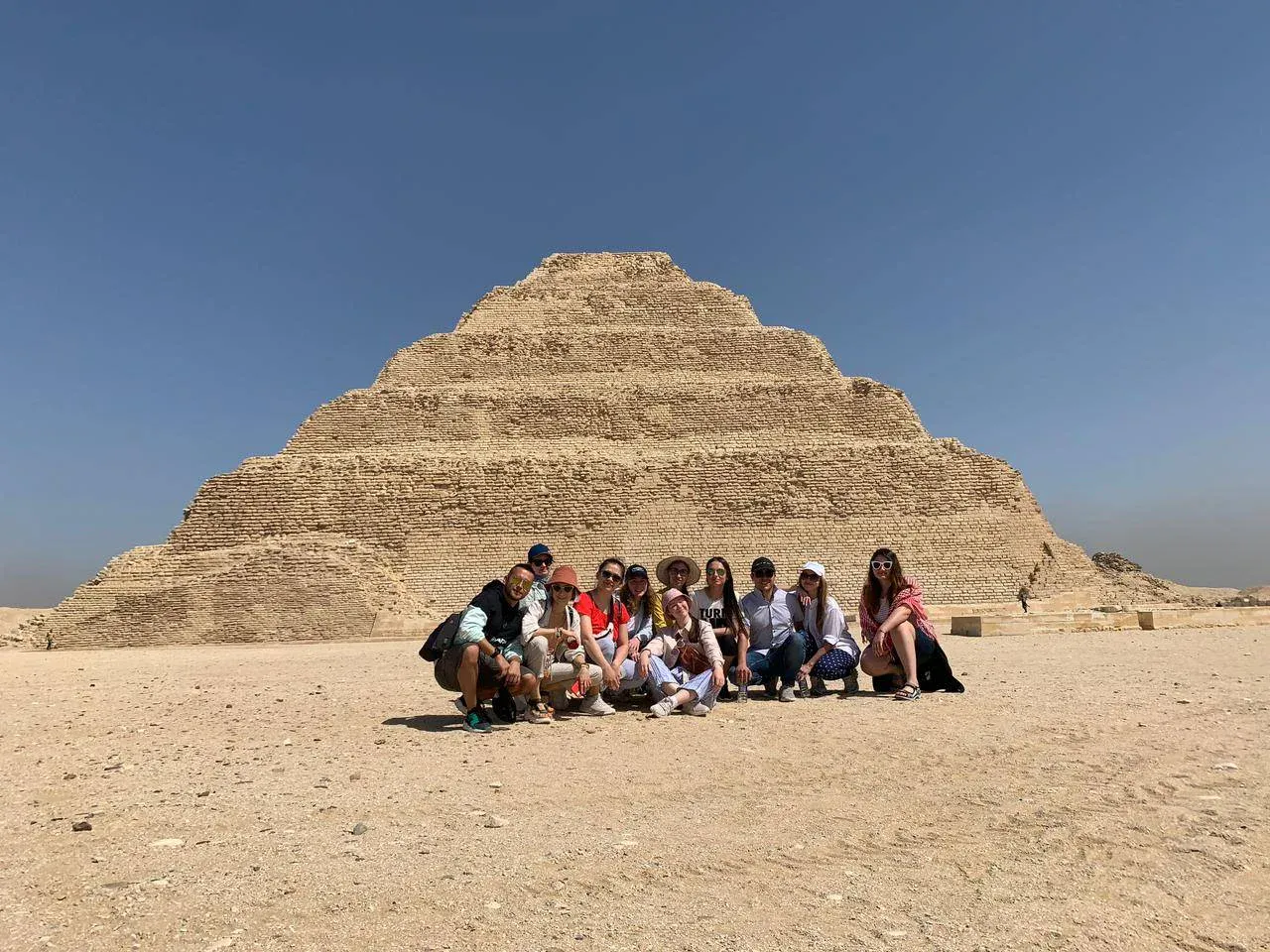 Groep toeristen poseert op het zand voor de trappenpiramide van Djoser in Sakkara