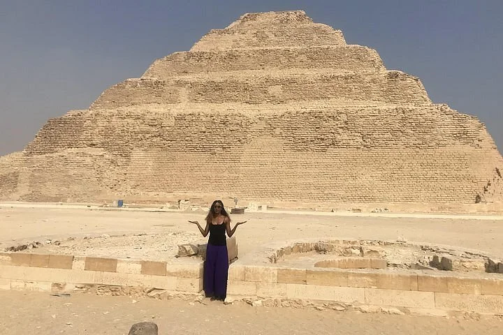 Vrouw poseert alleen met opgeheven armen voor de trappenpiramide van Djoser in Sakkara