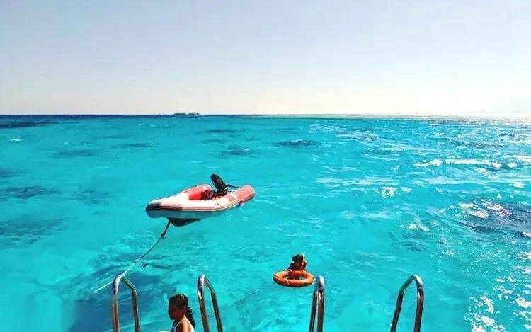 Vue depuis l'échelle de bain d'un bateau sur un petit annexe gonflable et une bouée rouge flottant sur une eau turquoise vif