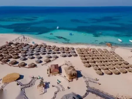 Légifelvétel egy strandklubról, ahol tucatnyi nádtetős napernyő sorakozik szép rendben egy türkizkék víz mellett