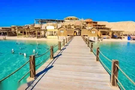 Fa móló vezet egy sekély türkiz lagúna feletti nádtetős strandépületek csoportjához, madarak pihennek a vízen