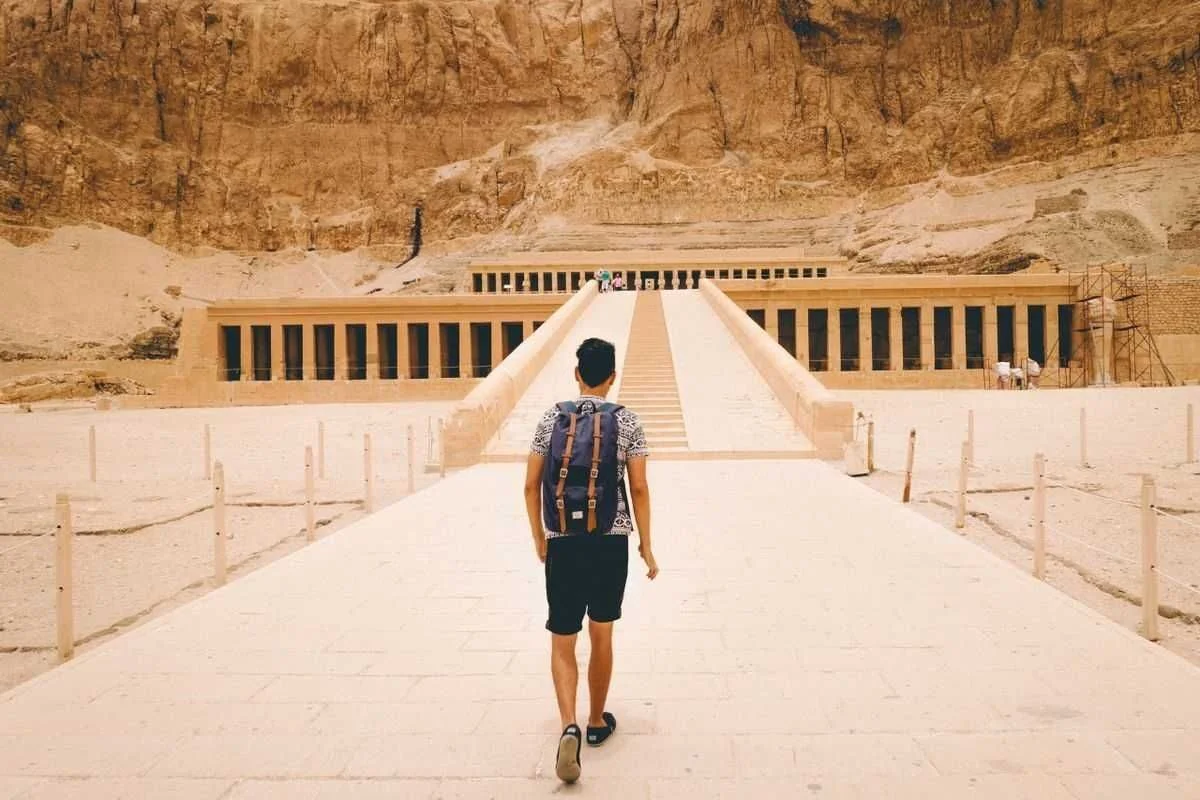 Homme avec un sac à dos marchant sur la rampe vers le temple d'Hatchepsout encastré dans les falaises