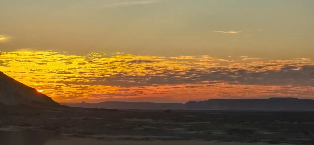 开阔的日落天空，橙色和金色的云条横跨深色沙漠地平线