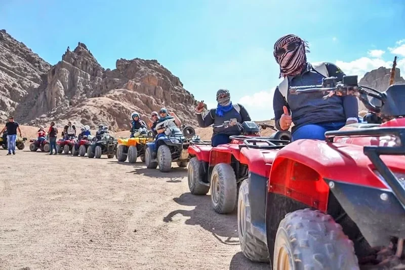 File de quads rouges avec pilotes en foulards du désert attendant dans une vallée montagneuse rocheuse