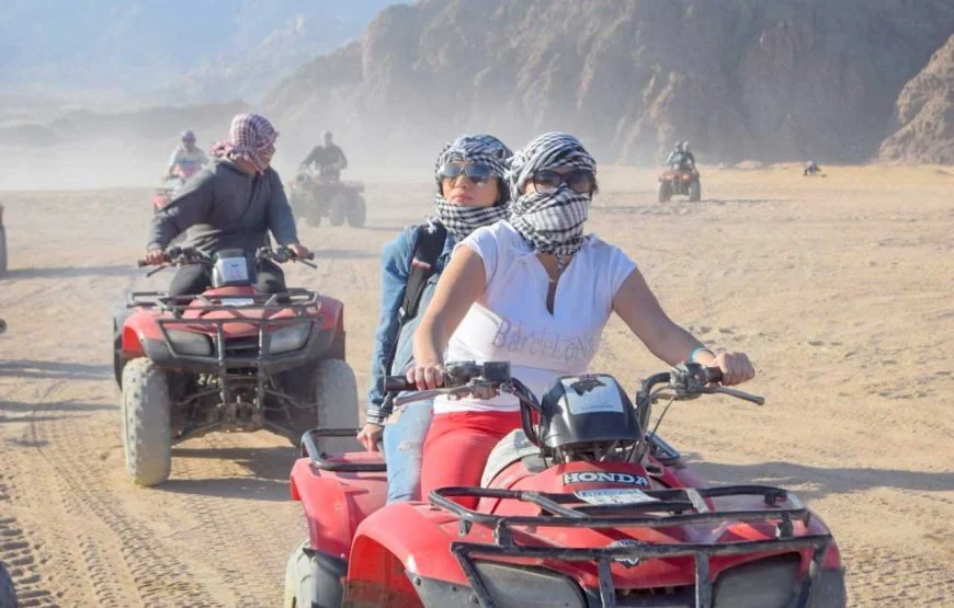 Deux femmes en chèches roulant ensemble sur un quad dans le désert, d'autres pilotes derrière elles