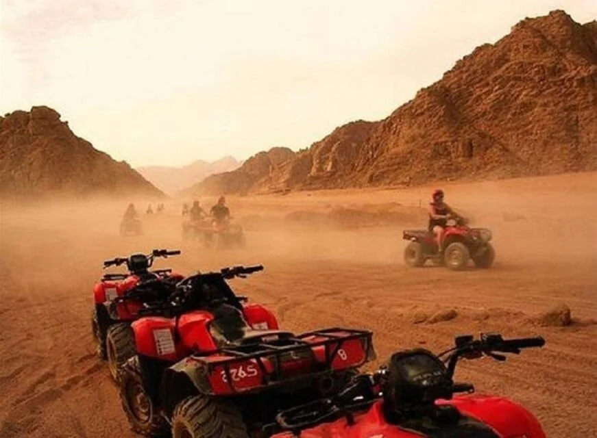 Gros plan de quads rouges alignés, pilotes partant dans un nuage de poussière dans une vallée montagneuse