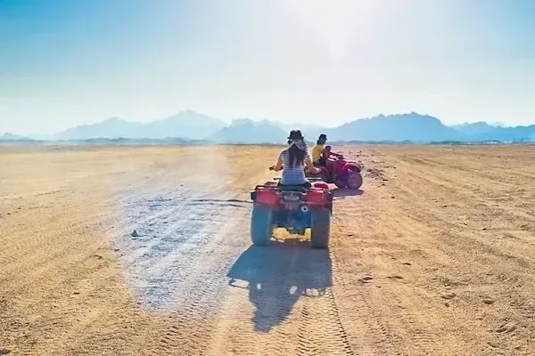 Quadrijders van achteren gezien die over vlak woestijnzand wegrijden richting verre bergen