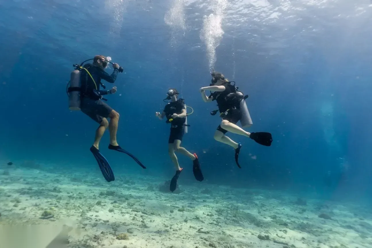 Trois plongeurs descendant ensemble en pleine eau au-dessus d'un fond sableux, bulles montant vers la surface