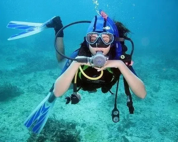 一位潜水员双手交叠漂浮在镜头前，脚蹼抬起，下方是珊瑚海床