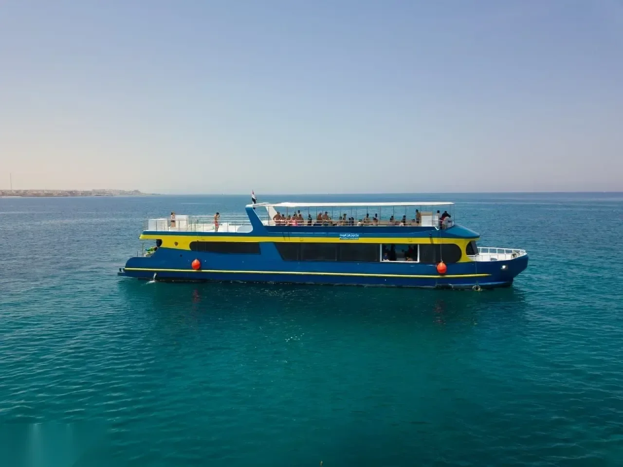 Blue and yellow semi-submarine passenger boat floating on turquoise water near a distant shoreline