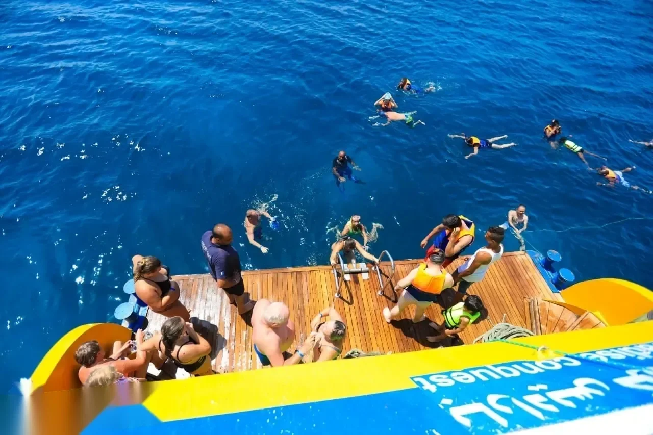 Aerial view from the boat's swim platform of snorkelers floating in deep blue water beside a wooden diving deck