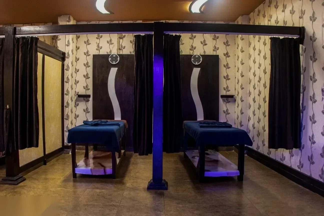 Schwach beleuchteter Hammam-Behandlungsraum mit zwei Massageliegen unter violettem LED-Licht und Vorhangnischen