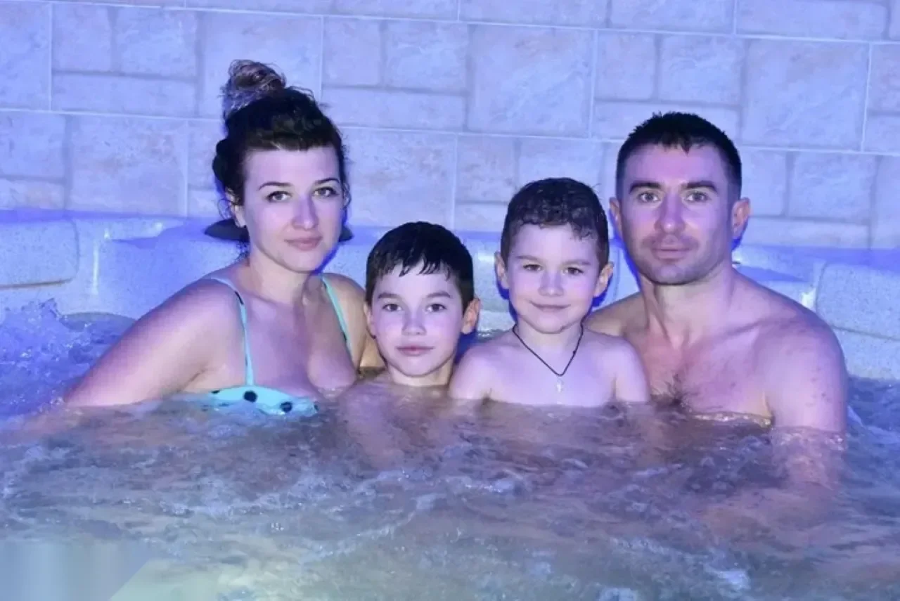 Familie mit vier Personen lächelt im sprudelnden Whirlpool mit gefliesten Steinwänden im violetten Licht