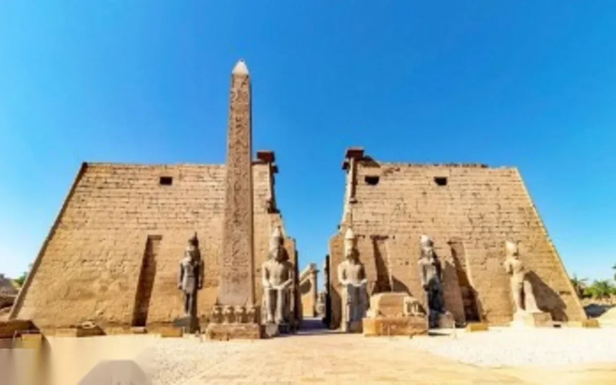 Eingangspylon des Luxor-Tempels mit sitzenden Pharaonenstatuen und hohem Obelisken vor klarem blauem Himmel