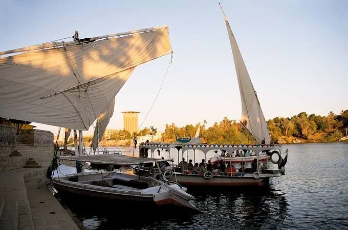 Feloeken afgemeerd aan een stenen oeverkade in Aswan met stadsgebouwen erachter