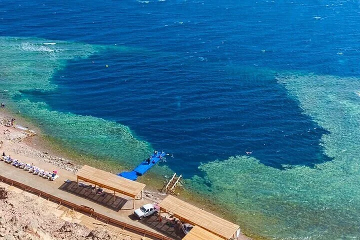 Vue aérienne d'un spectaculaire lagon bleu et d'un trou de récif près d'un petit ponton en bois et d'un camp de plage