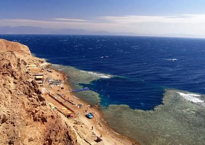 Vue aérienne côtière : récif turquoise peu profond rejoignant la pleine mer bleu profond le long d'un rivage désertique