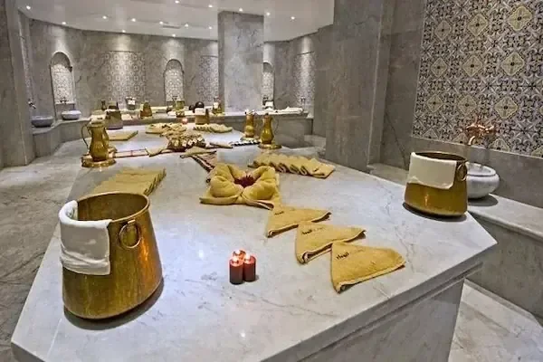 Marmor-Hammamtisch mit dekorativ gefalteten goldenen Handtüchern, Messingeimern und brennenden Kerzen