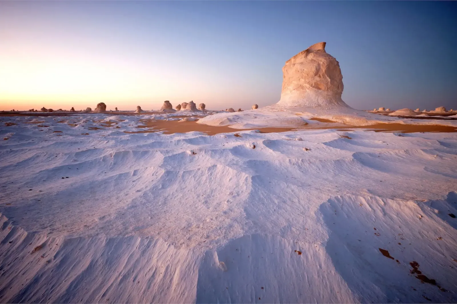 Hoher pilzförmiger Kalkfelsen auf hellweißem Boden unter Abendhimmel in der Weißen Wüste