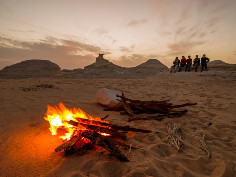 Feu de camp sur le sable au crépuscule avec le groupe au loin dans le Désert Blanc