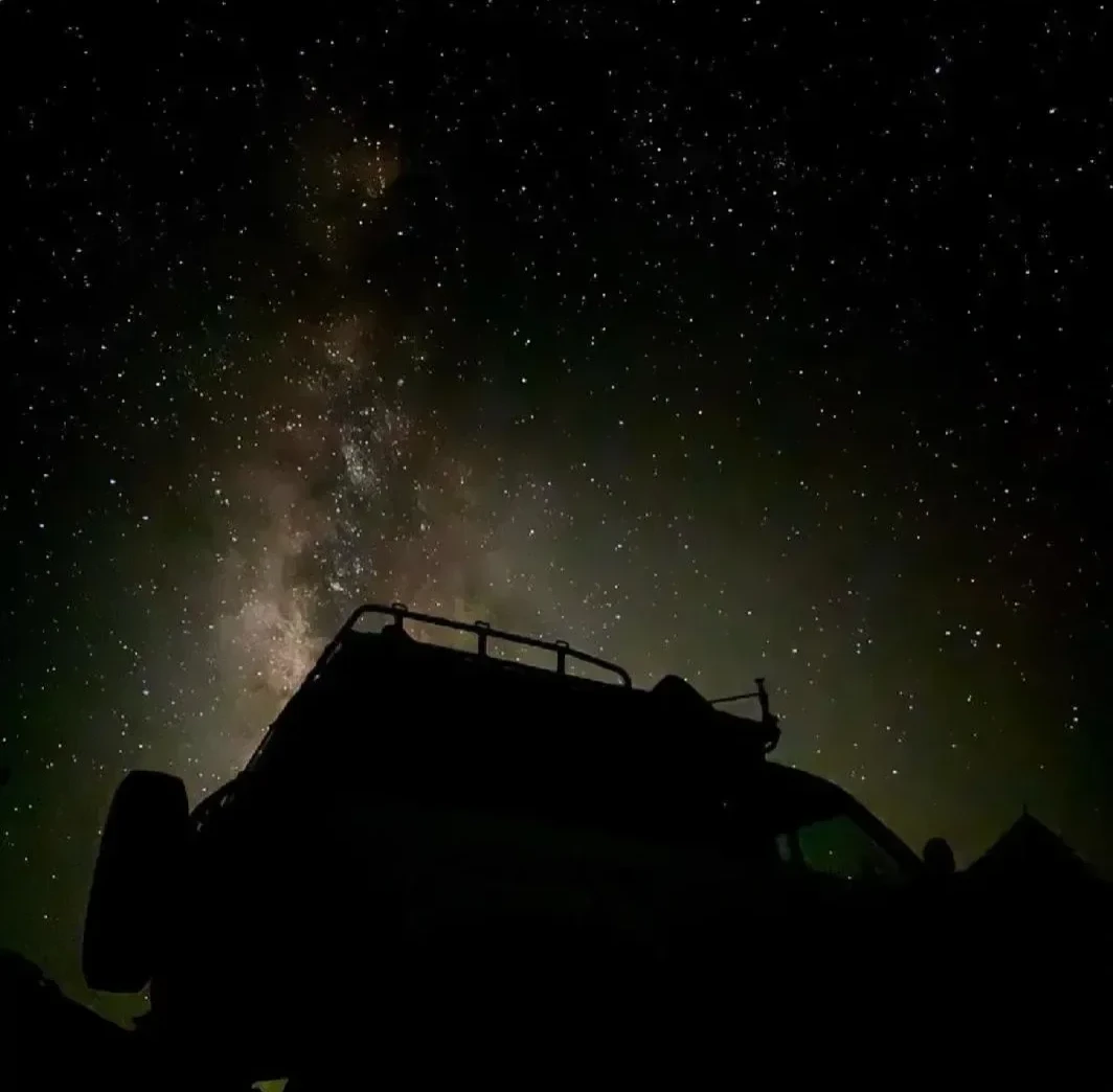 Силуэт багажника сафари-внедорожника 4x4 на фоне ночного неба, полного звёзд, с Млечным Путём над пустыней