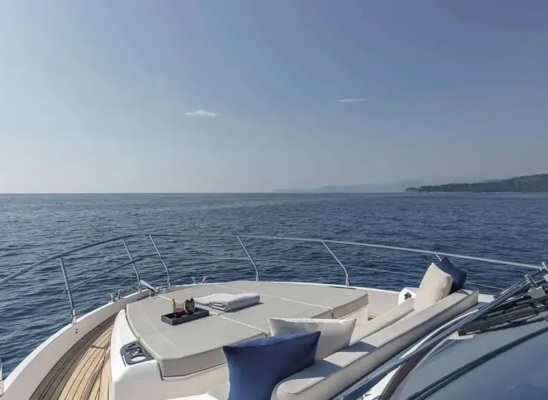 Empty bow deck of a white luxury yacht with cream cushioned loungers and navy blue pillows